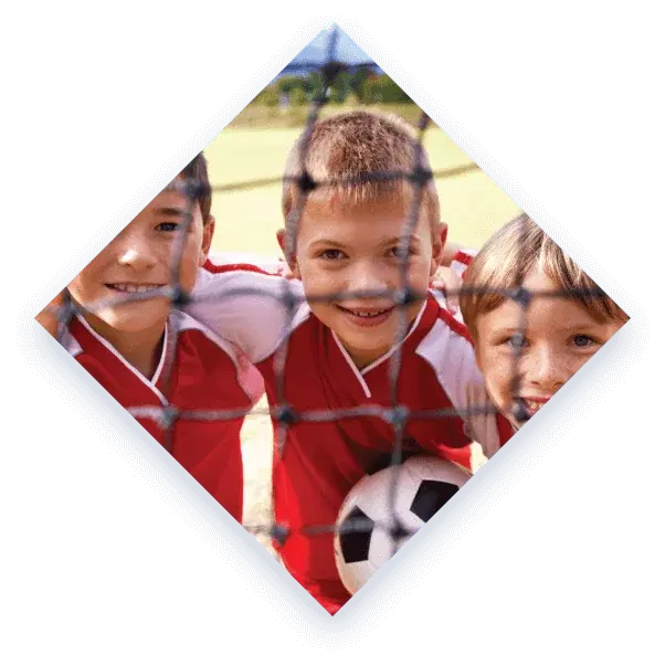 Three smiling boys in football kit behind a goal net